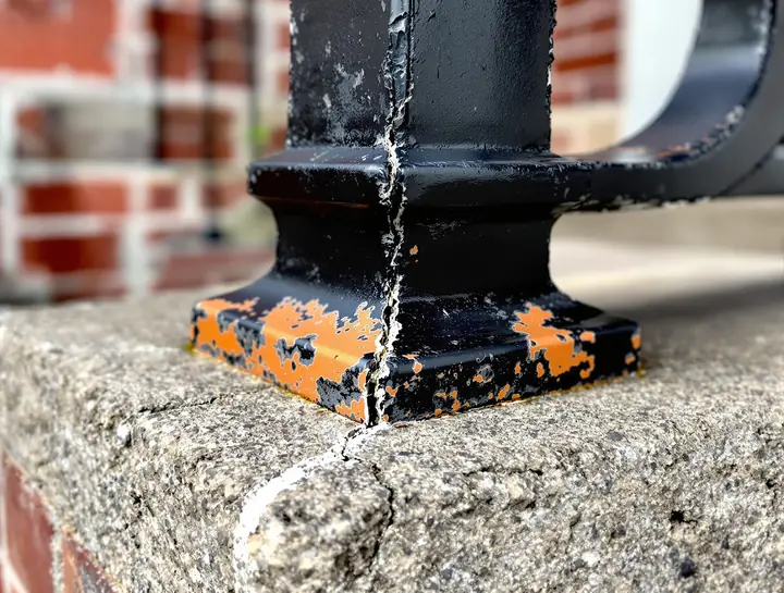 Illustrative photo: flaking paint and rust at the base of an iron railing post on a concrete step